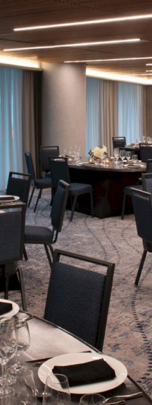 The image shows an elegantly set banquet hall with round tables covered in black linens, set with dinnerware and glasses, and decorated with floral arrangements.